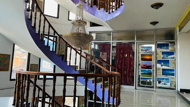 A spiral staircase with wooden railings and a chandelier, leading to a second floor. - Hotel Centre Point (Srinagar)