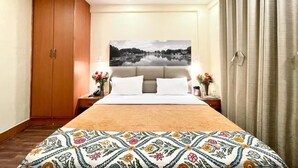 A bedroom with a bed, a nightstand, a wardrobe, and a large window with curtains. - Hotel Centre Point (Srinagar)
