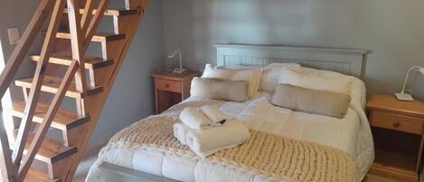A bedroom with a wooden ladder, a bed with white bedding, a bedside table with a lamp, and a nightstand with a phone.