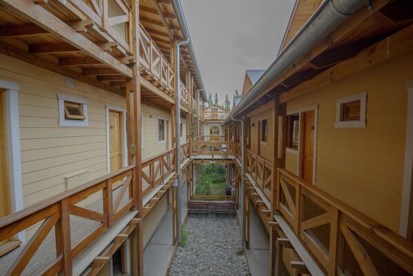 A corridor with wooden railings and a gravel path leading to a central area with a view of trees.
