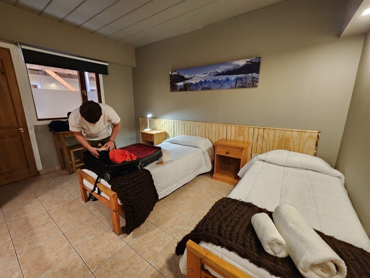 Ett hotellrum med två sängar, en sänggavel i trä, ett nattduksbord, en lampa och en tavla på väggen.