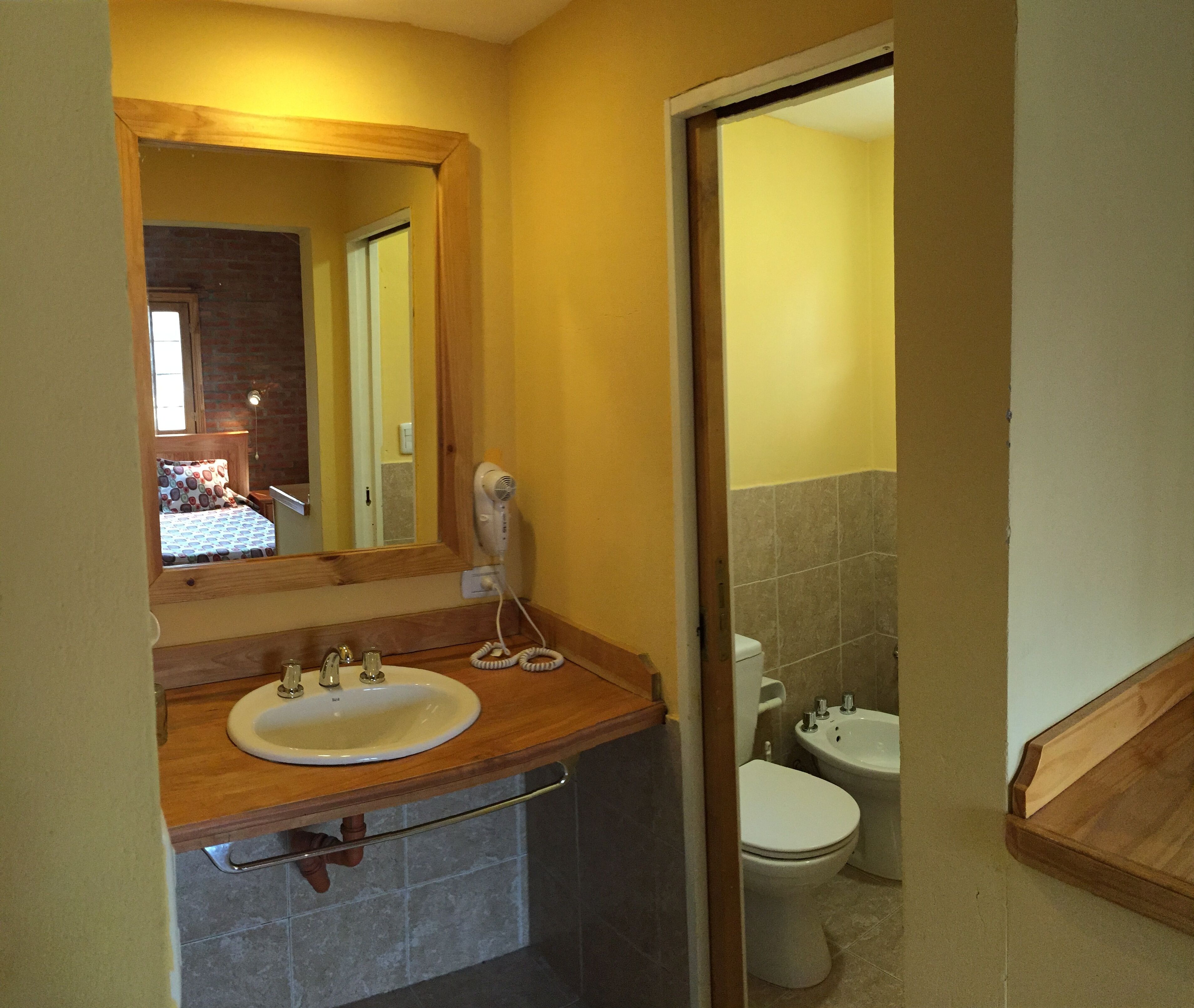 Ein Badezimmer mit einem Holzkosmetikschrank, einem Waschbecken, einem Spiegel, einem Fön und zwei Toiletten.