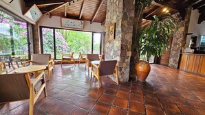 A rustic interior with stone walls, wooden furniture, and large windows overlooking a garden. - Hotel Selva Montana (Villa San Lorenzo)