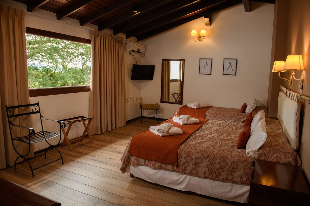 A bedroom with a bed, a chair, a TV, and a window with curtains.