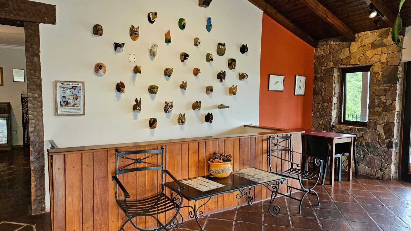 A reception area with a wooden bench, metal chairs, and a wall displaying various animal masks.