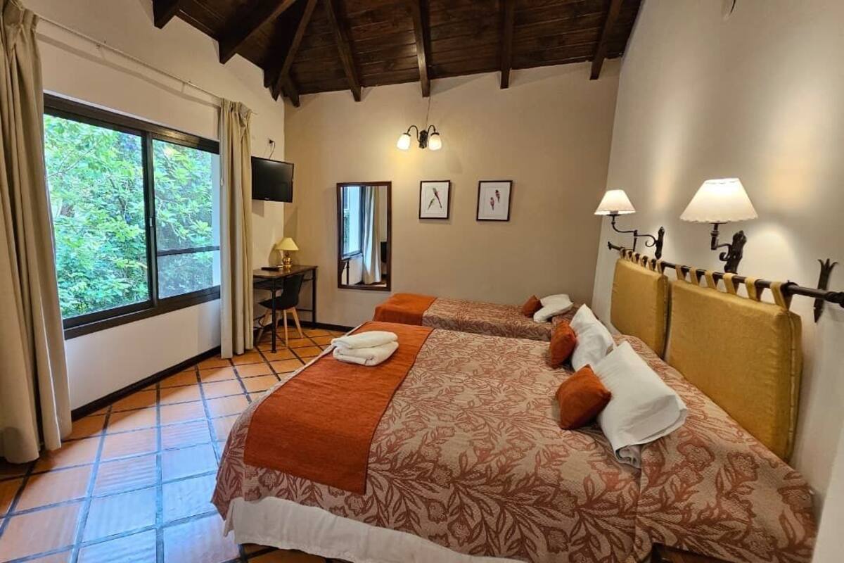 A bedroom with two beds, a desk, a chair, and a window with curtains.