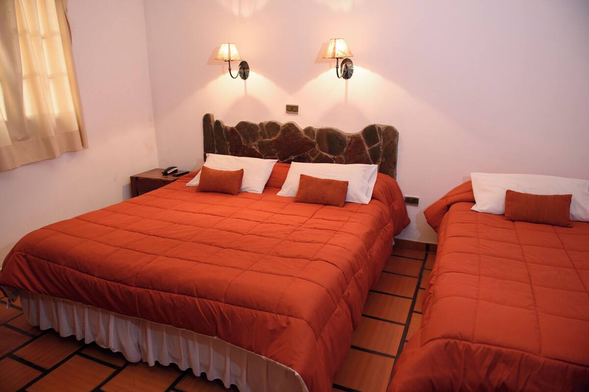 A hotel room with two beds, each with an orange bedspread and white pillows. There are two wall-mounted lamps on either side of the headboard.