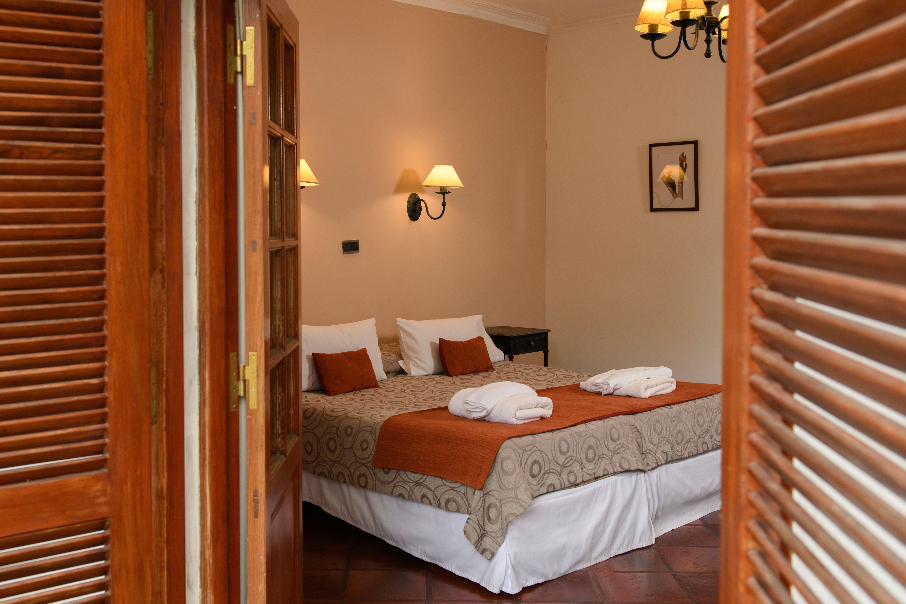 A hotel room with a bed, a nightstand, wall-mounted lamps, and a framed picture on the wall.