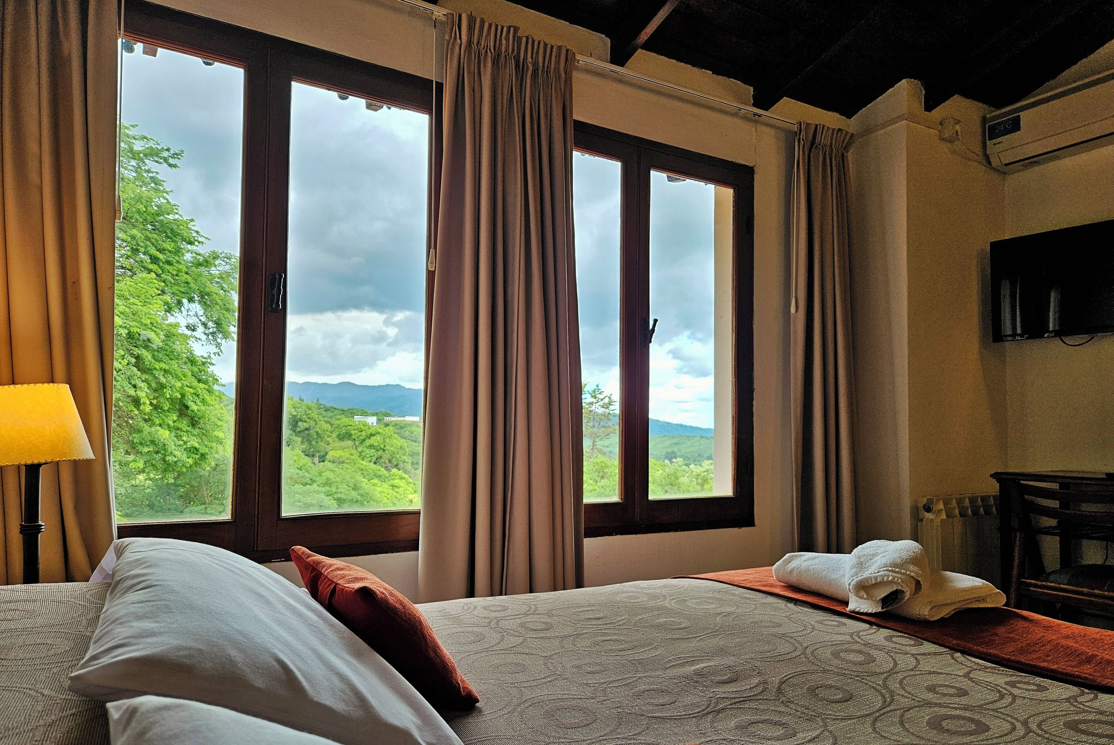 A hotel room with a bed, a view of the outdoors, and a television on the wall.
