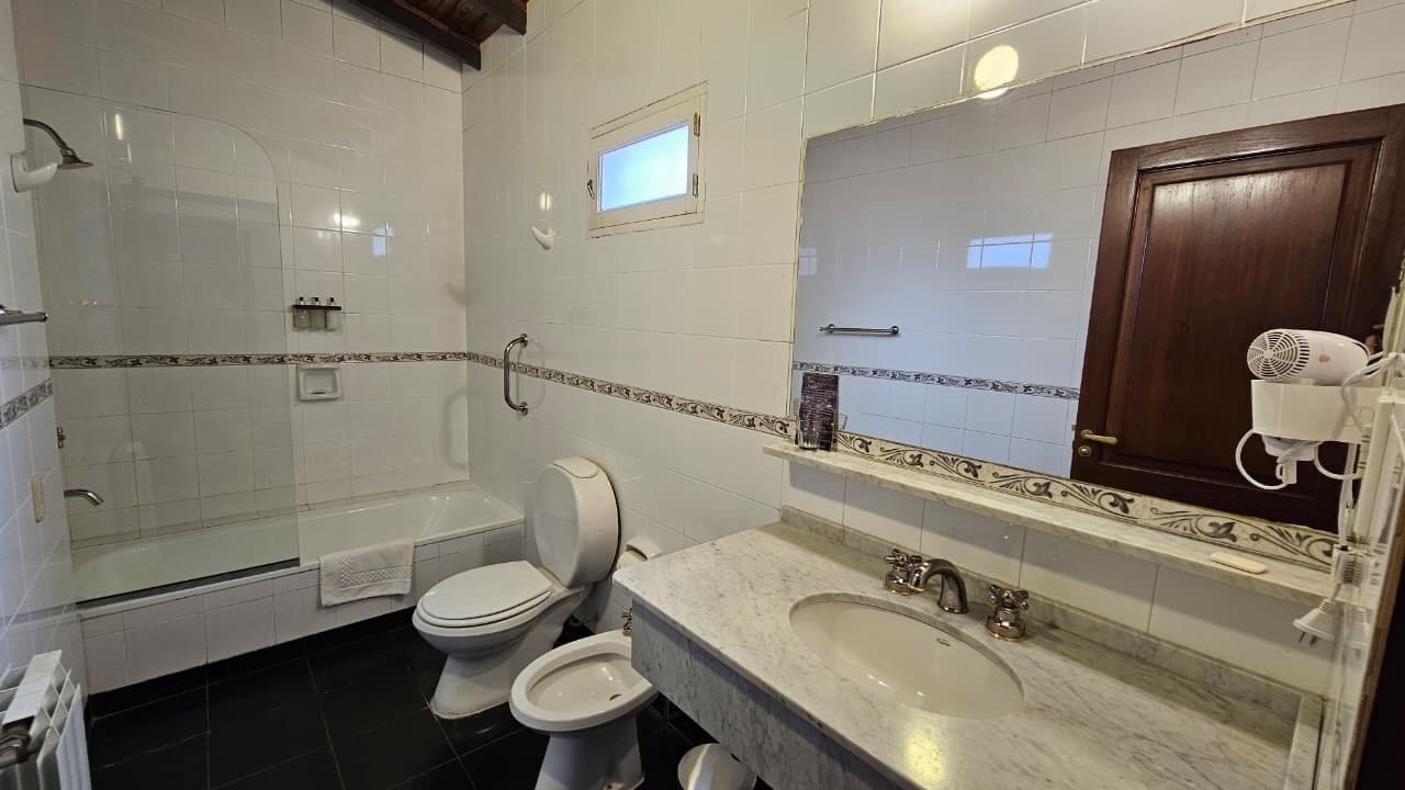 Baño con ducha, inodoro, bidé y tocador con lavamanos y espejo.