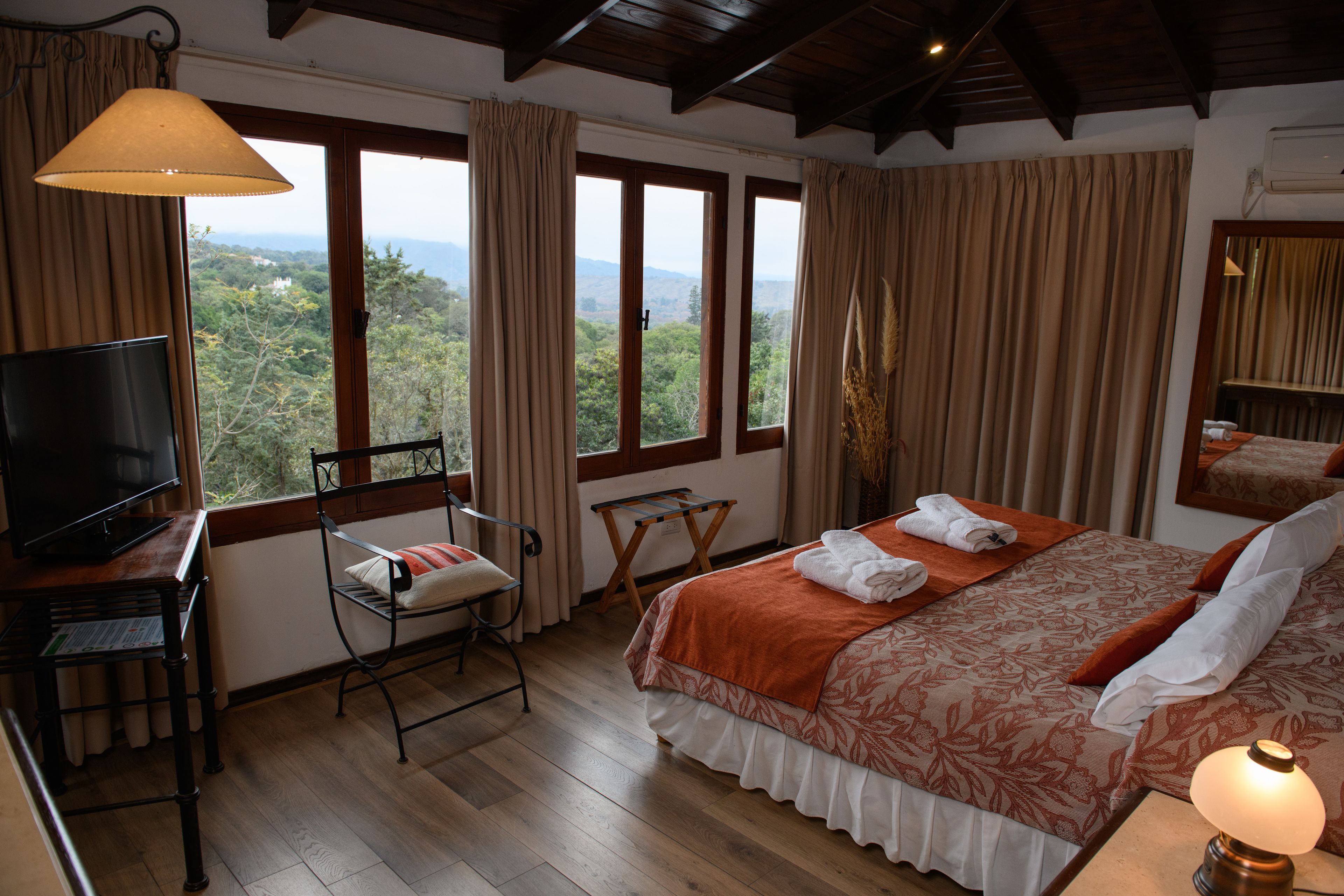 A bedroom with a bed, a TV, a chair, and a view of the outdoors.
