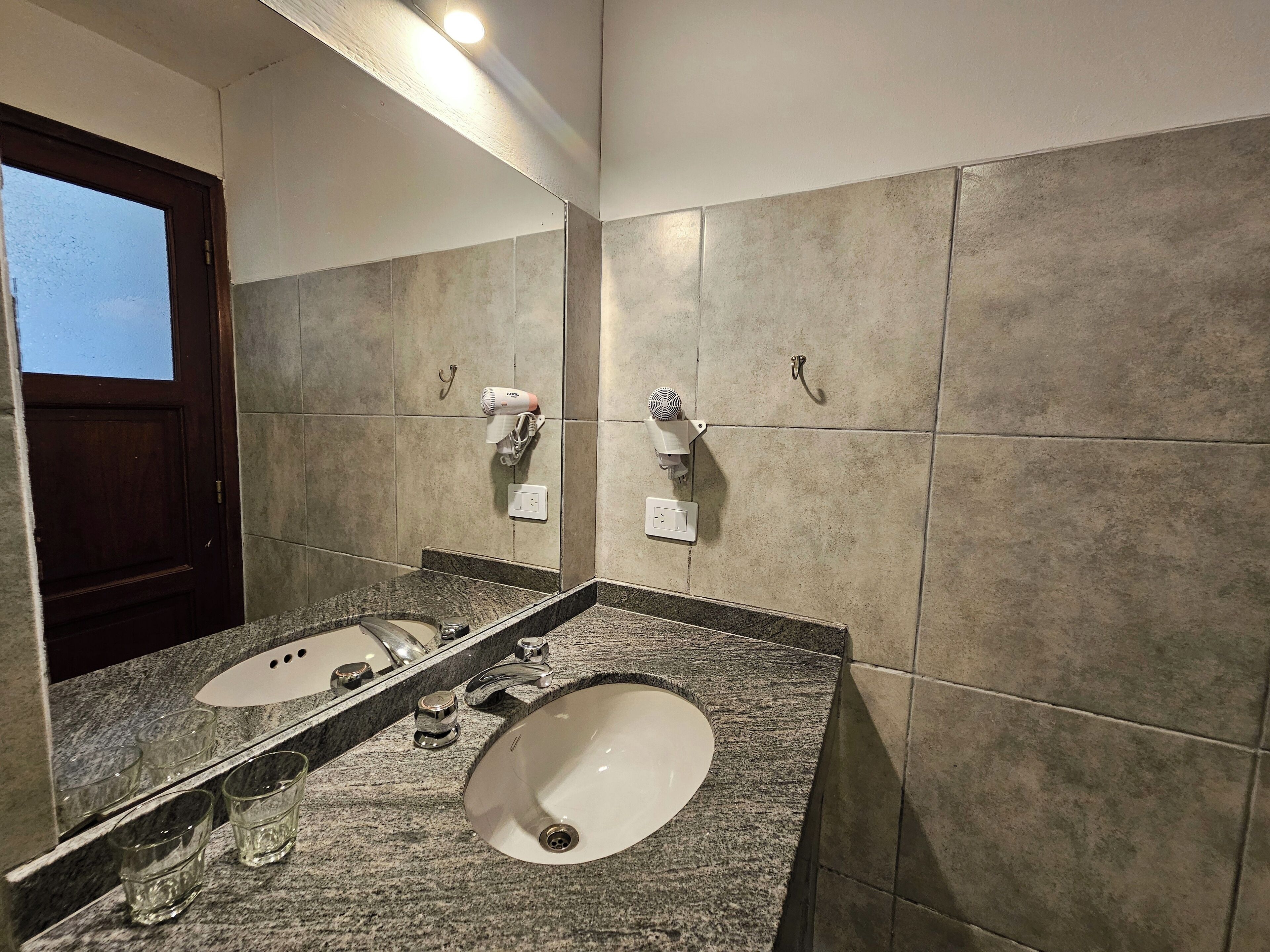 A bathroom with two sinks, a mirror, and a hairdryer mounted on the wall.
