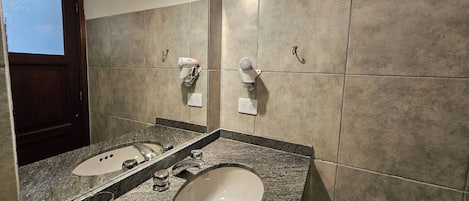 A bathroom with two sinks, a mirror, and a hairdryer mounted on the wall.