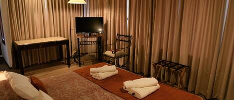 A hotel room with a bed, a desk, a chair, a TV, and curtains.