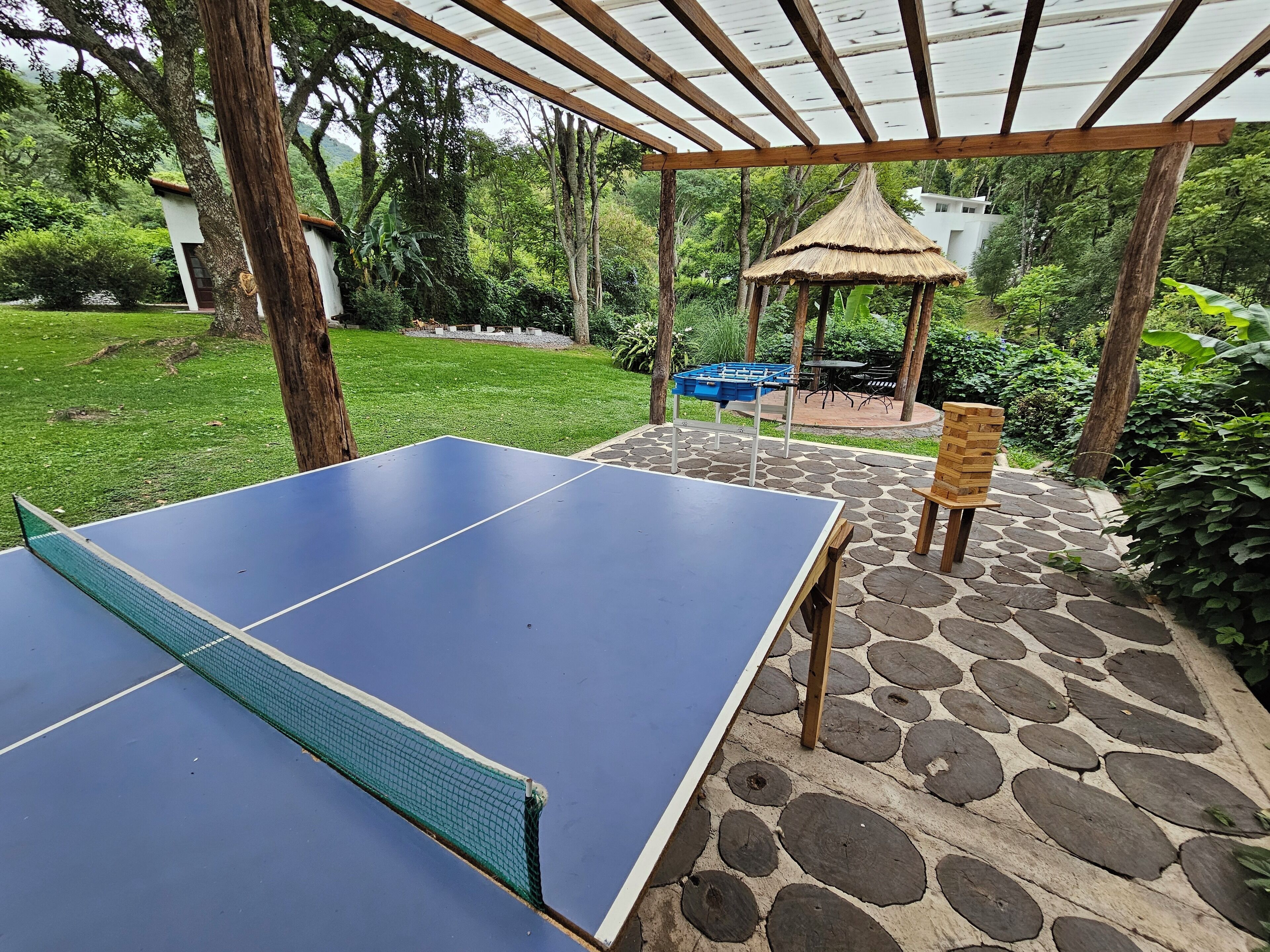 A ping pong table in a covered outdoor area with stone flooring and a gazebo in the background.