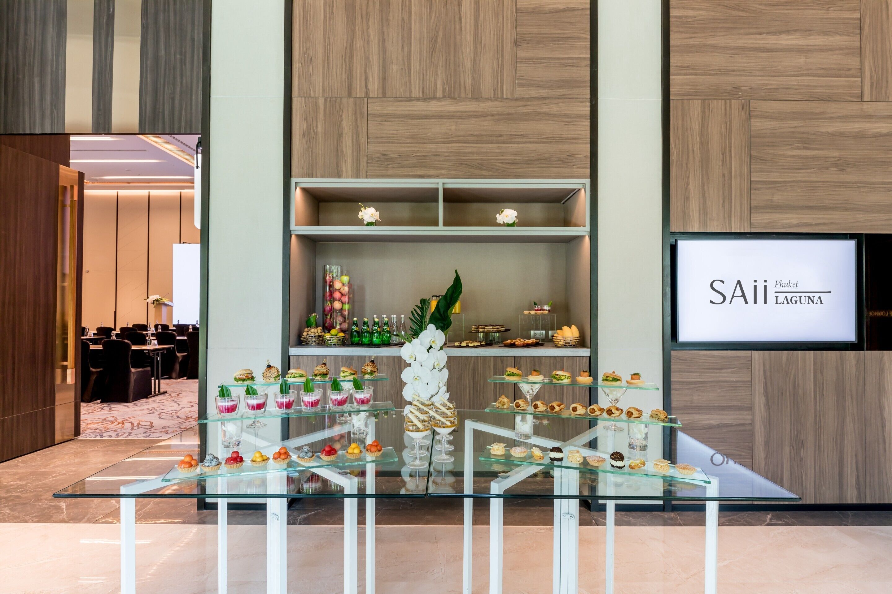A modern hotel lobby with a glass display of desserts and a sign reading "SAii Phuket Laguna".