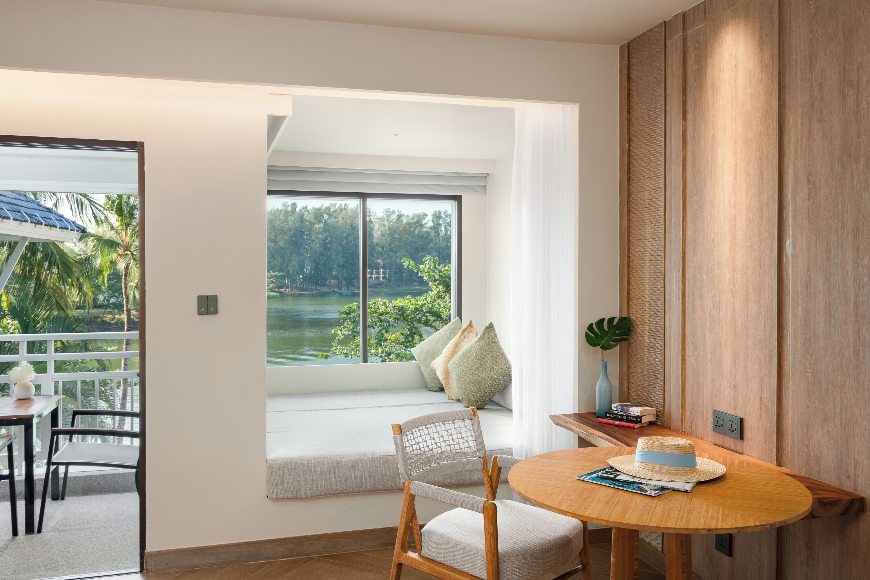 A room with a large window, a wooden table, a chair, and a small balcony area.