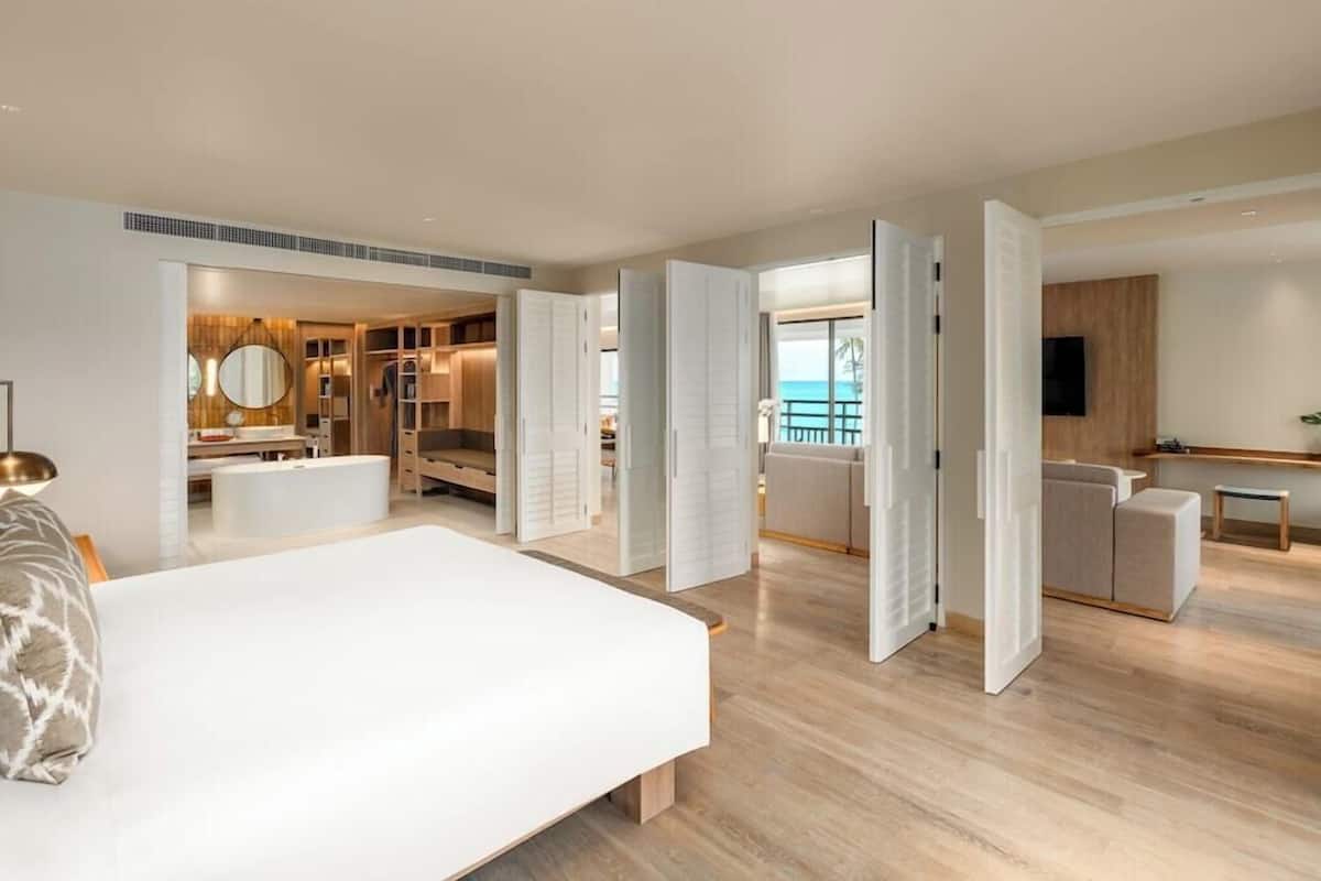 A modern hotel room with a large bed, a walk-in closet, a kitchenette, and a balcony with a view.