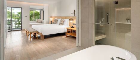 A modern hotel room with a large bed, a sitting area with a bench, a glass-enclosed shower, and a bathtub.
