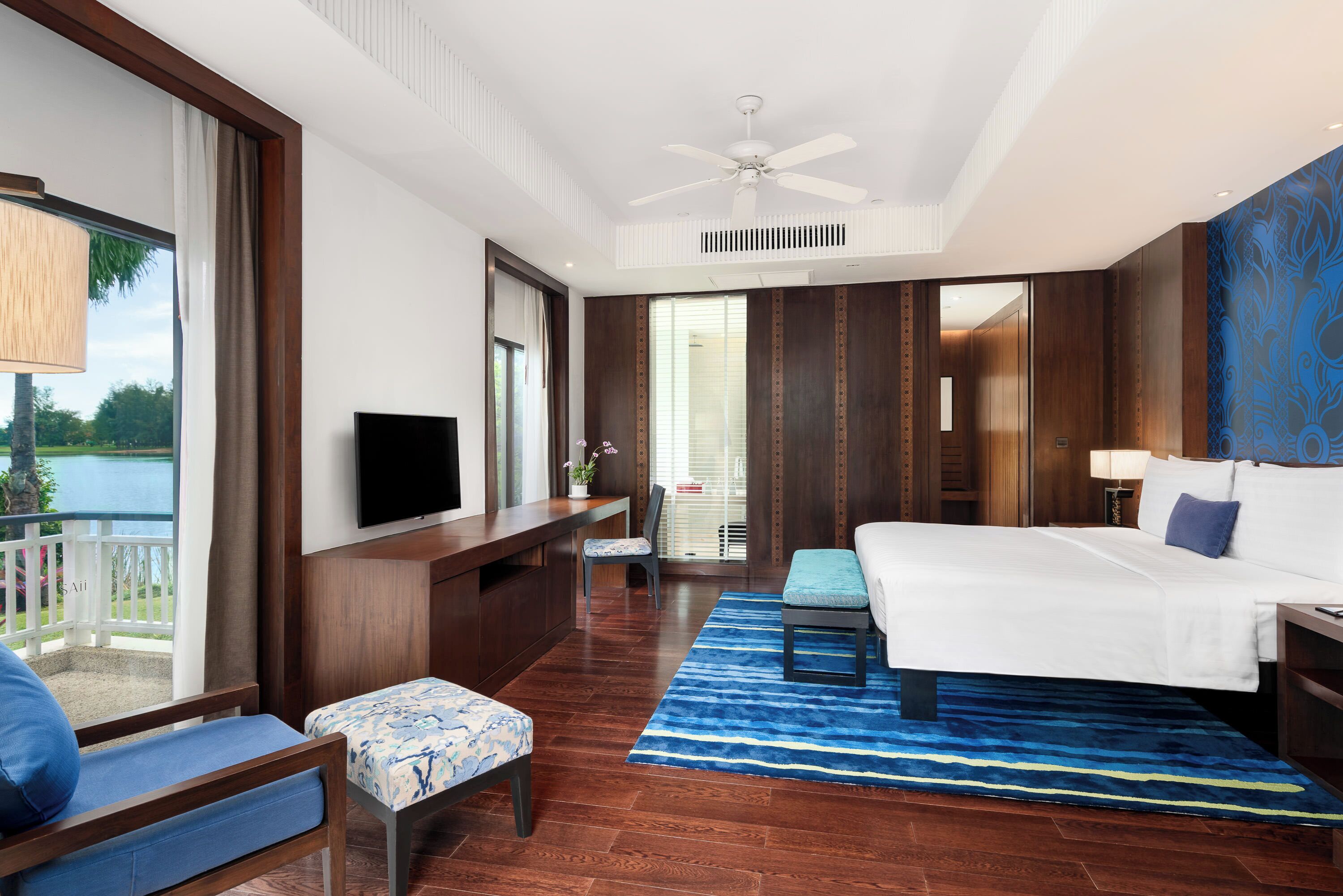 A hotel room with a bed, a desk, a TV, a chair, and a view of the outdoors.