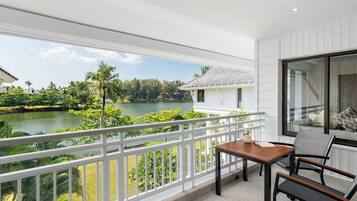 A balcony with a view of a lake, white railings, and a table with chairs.
