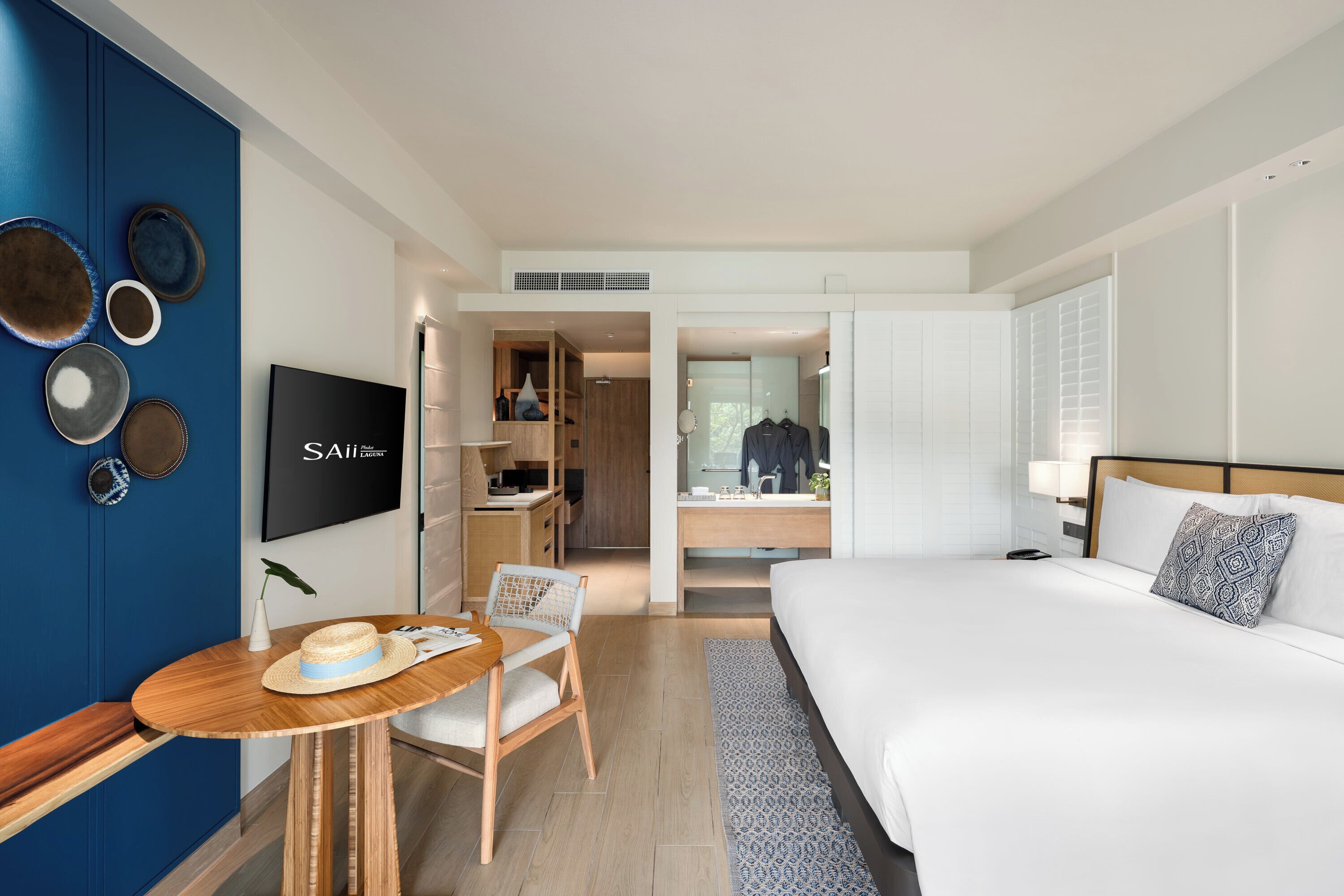 A modern hotel room with a large bed, a TV, a desk with a chair, and a wardrobe.