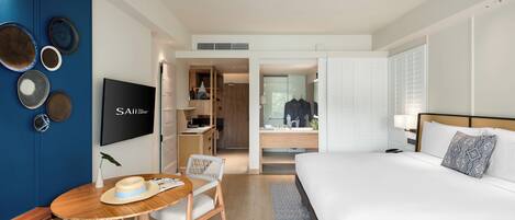 A modern hotel room with a large bed, a TV, a desk with a chair, and a wardrobe.