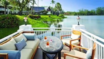 A balcony with a sofa, chairs, and a table with drinks, overlooking a lake and a resort building.