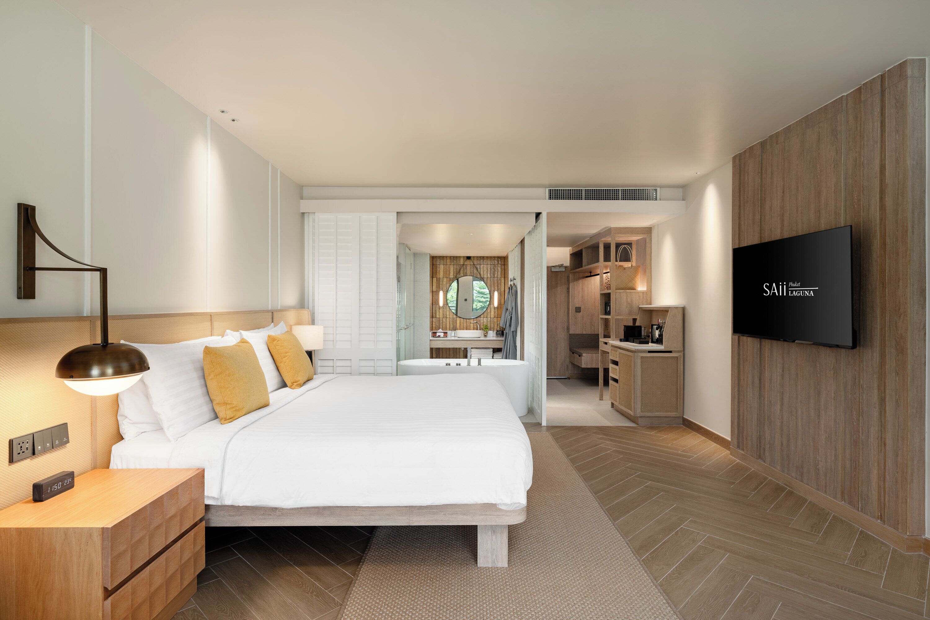 A modern hotel room with a large bed, bedside tables, a TV, and a bathroom visible through an open door.