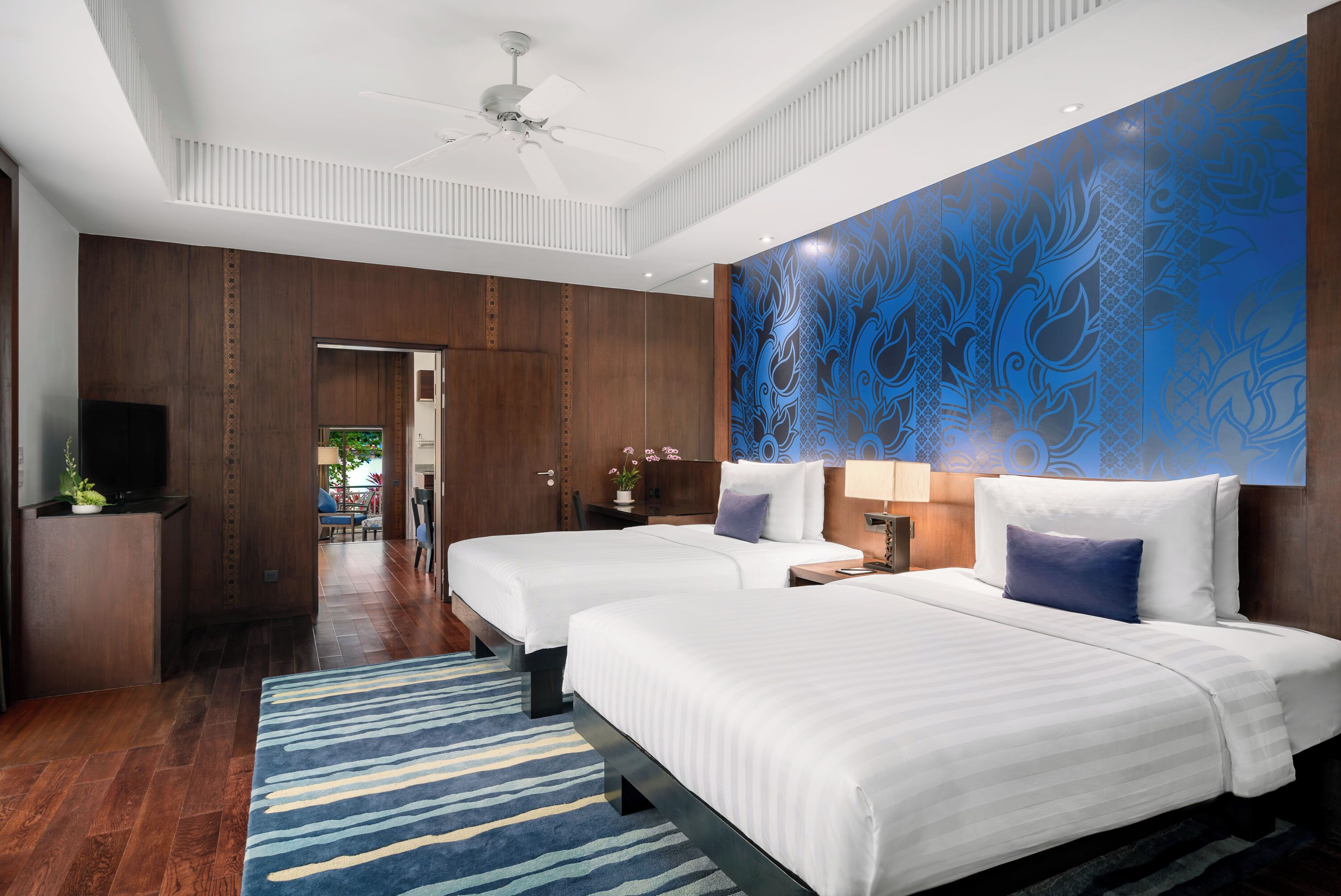Une chambre d’hôtel avec deux lits, un grand mur décoratif et une vue sur un couloir.