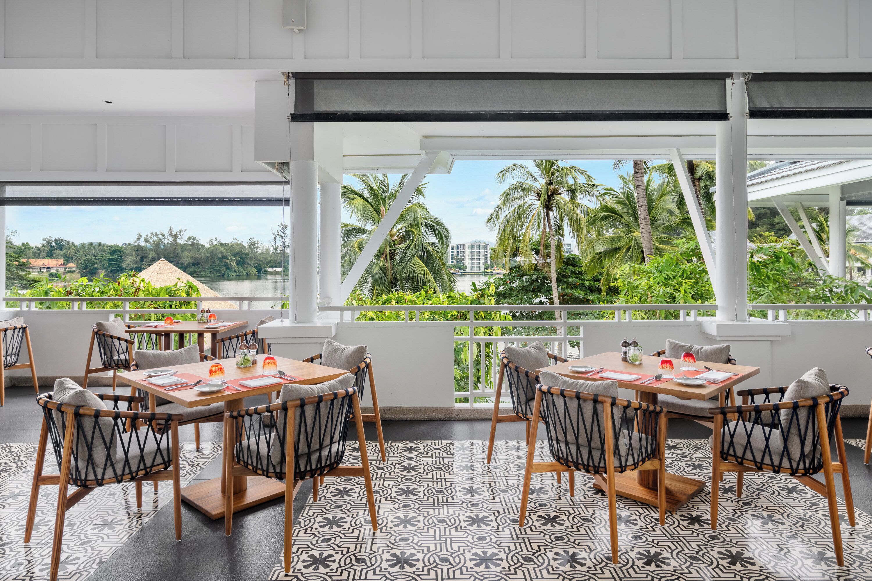 Un comedor con mesas y sillas, ventanas amplias con vistas a palmeras y edificios.