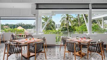 Un comedor con mesas y sillas, ventanas amplias con vistas a palmeras y edificios.