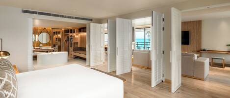 Una habitación de hotel moderna con una cama grande, un vestidor, un baño con bañera y un balcón con vistas al océano.