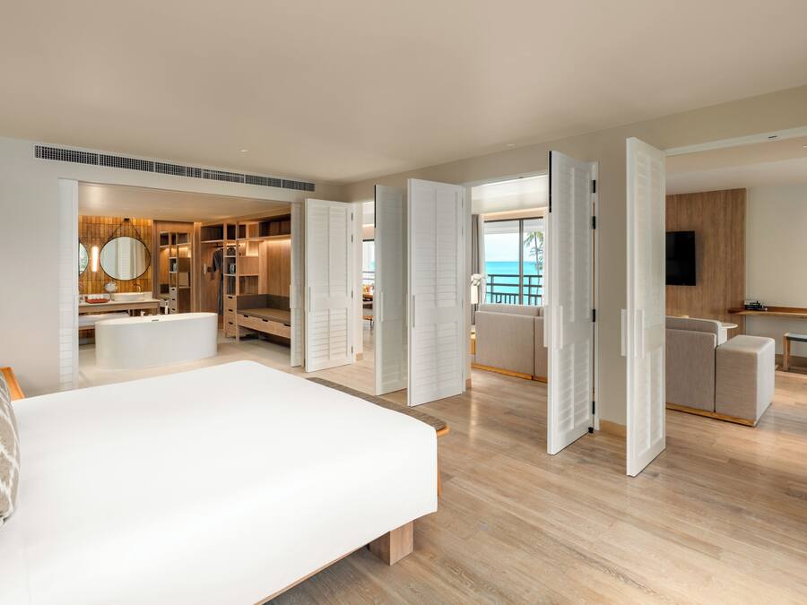 Una habitación de hotel moderna con una cama grande, un vestidor, un baño con bañera y un balcón con vistas al océano.
