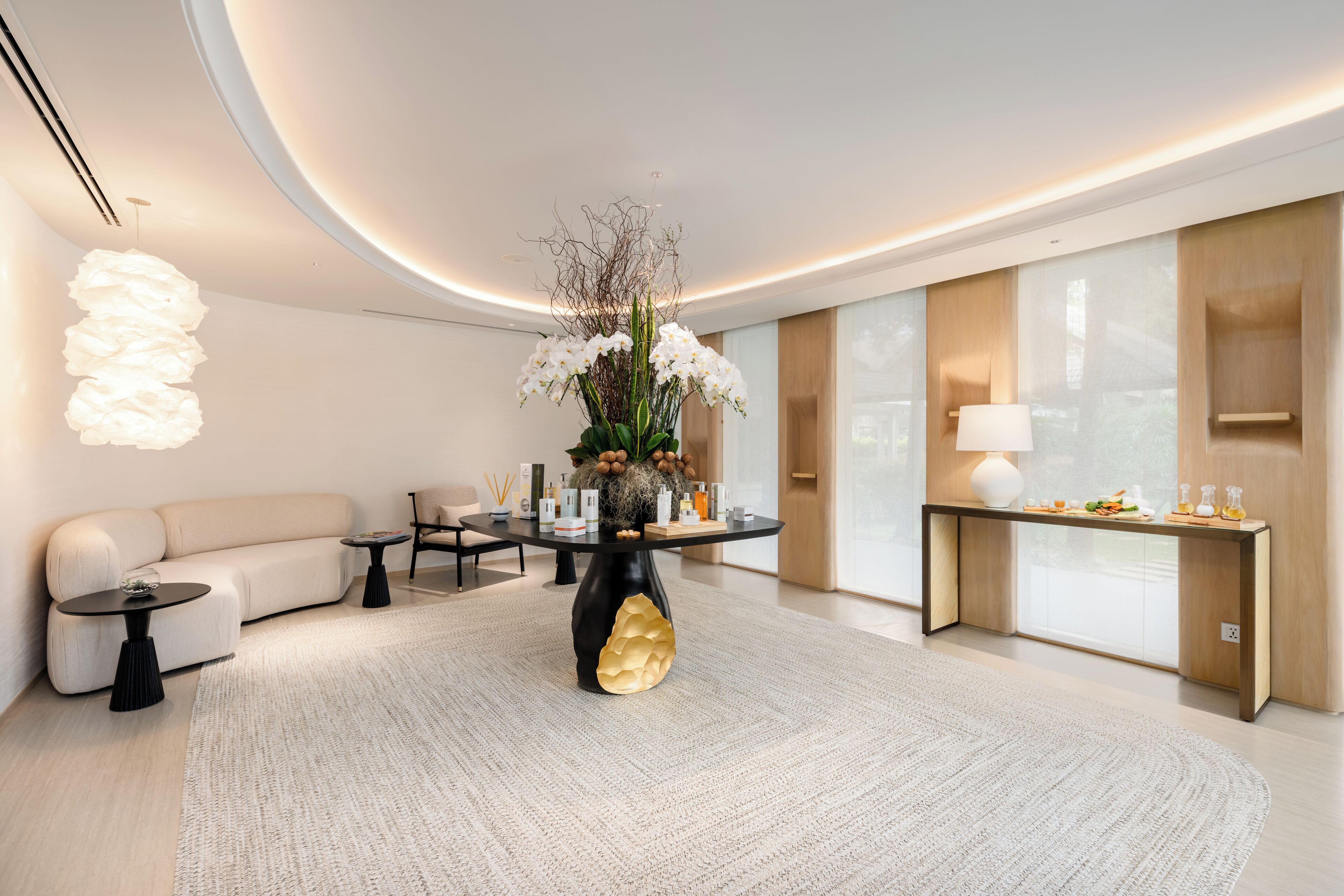 A modern living room with a round coffee table, a sofa, a decorative vase with flowers, and a console table with a lamp.