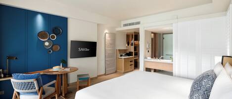 Una habitación de hotel moderna con una cama grande, un escritorio con silla, un televisor y una kitchenette.