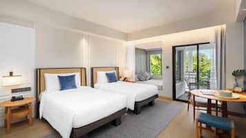 Ein Hotelzimmer mit zwei Betten, einem kleinen Tisch, einem Stuhl und einem Balkon mit Blick auf Grünflächen.