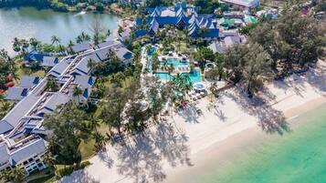 Vista aérea de un resort con varias edificaciones, un amplio espacio de piscina y una playa.