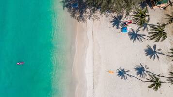 An aerial view of a beach with clear turquoise water, a few palm trees, and a small boat.