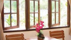 Ein Zimmer mit Holztisch und zwei Stühlen, einem fenster mit Vorhängen und Blick ins Grüne.