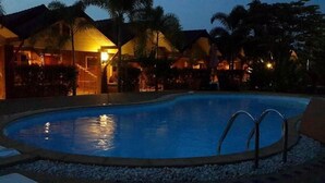 Ein Pool, umgeben von Palmen und Gebäuden mit warmer Beleuchtung.