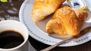 Une assiette avec deux croissants, un petit pot de beurre et une tasse de café, le tout posé sur une table.