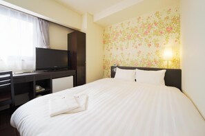 Habitación de hotel con cama, escritorio con televisor, lámpara y papel tapiz floral.