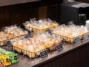 A bakery display with various pastries in clear plastic bags, labeled with names like "Curry Danish" and "Chocolate Danish."