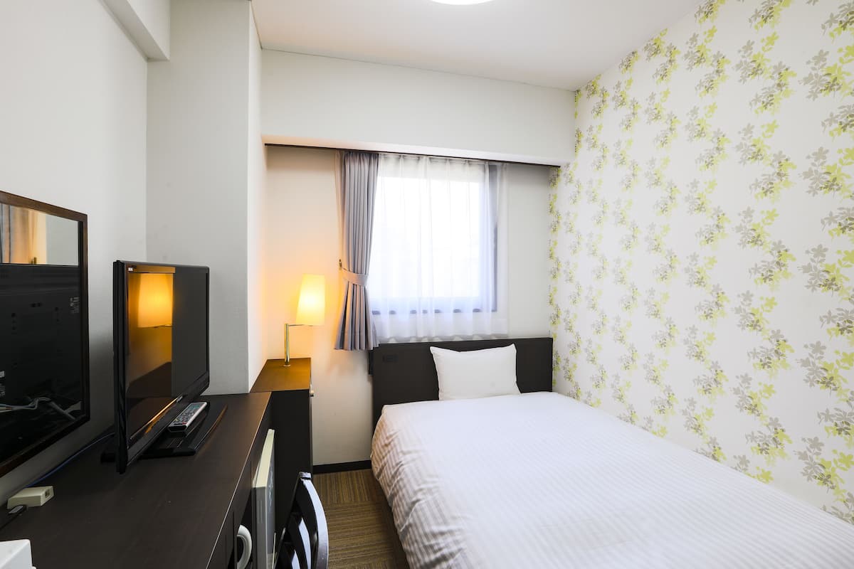 A hotel room with a bed, a desk with a television, and a window with curtains.