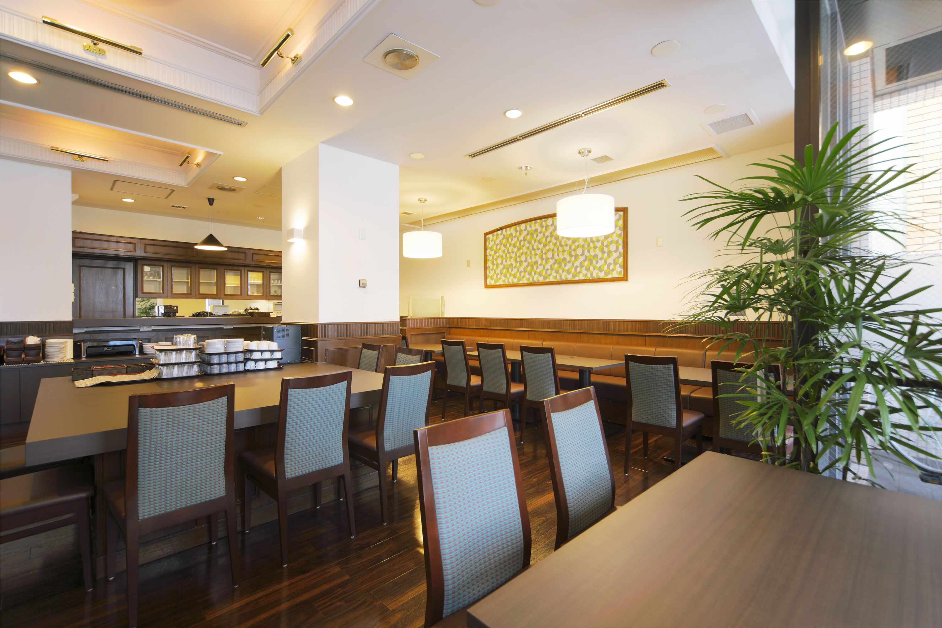 A restaurant with a long counter, multiple tables, and chairs. There is a kitchen area in the background.