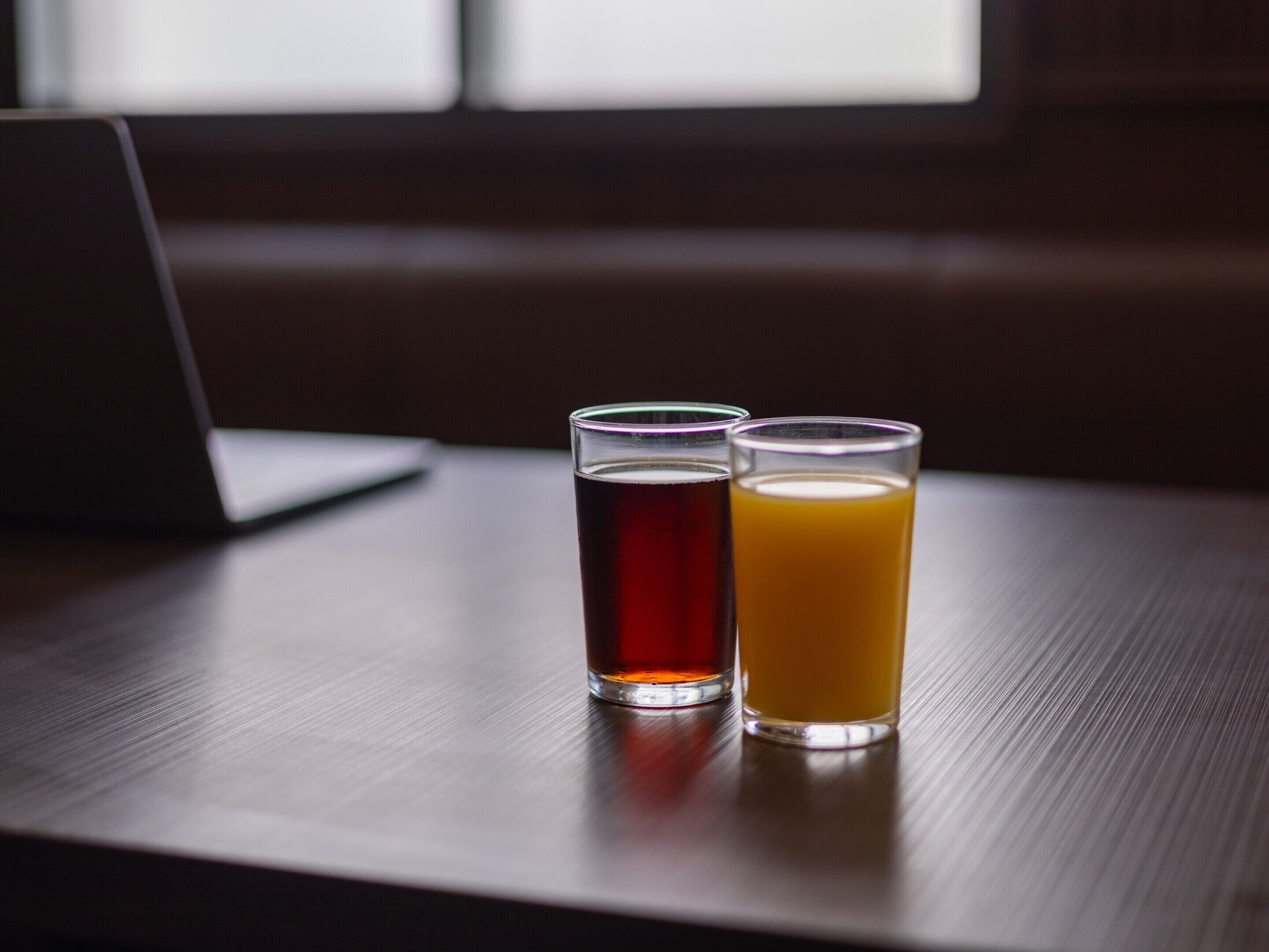 Dos vasos de bebidas sobre una mesa de madera con un ordenador portátil.