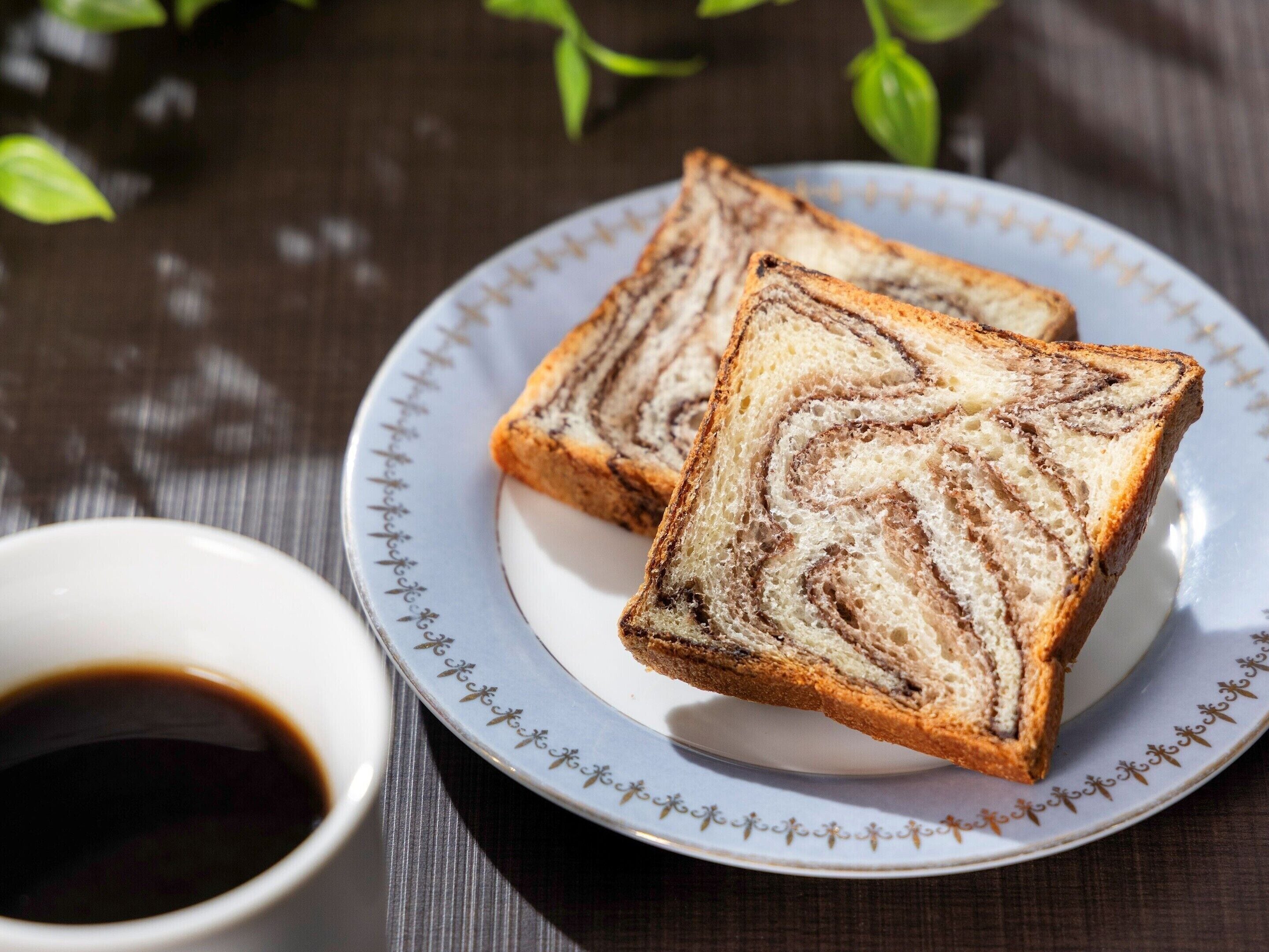 Zwei Scheiben Marmeladenbrot liegen auf einem Teller, daneben eine Tasse Kaffee.
