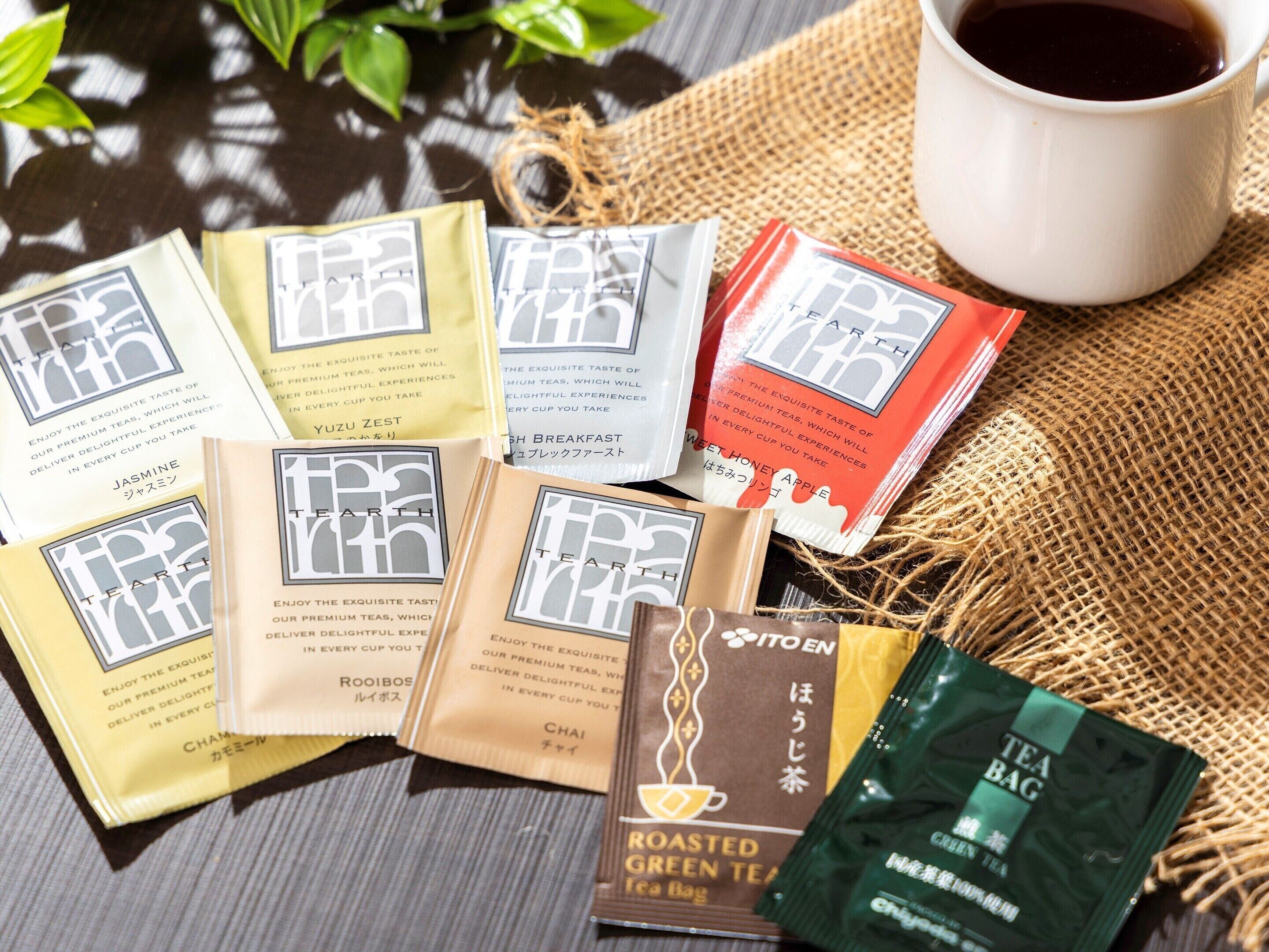 A variety of tea bags and a cup of tea on a burlap surface.