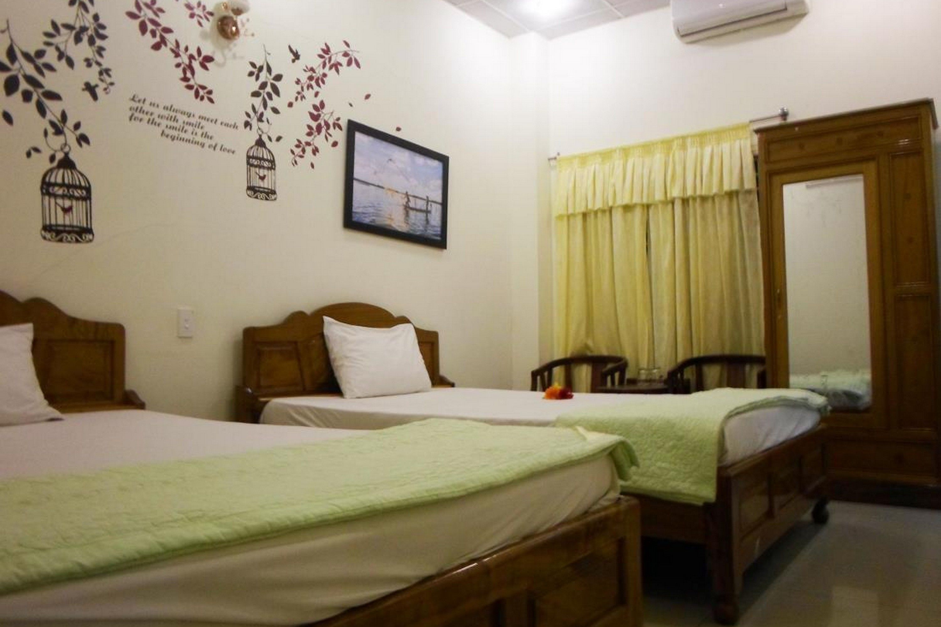 A hotel room with two single beds, a wooden wardrobe, a mirror, and a wall decoration.